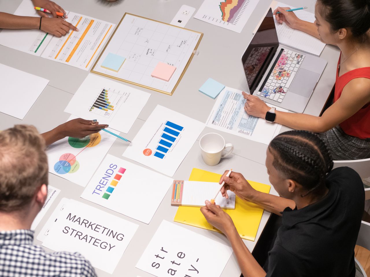 Vue en plongée d’une équipe diverse analysant des stratégies marketing à l’aide de graphiques et de tableaux.